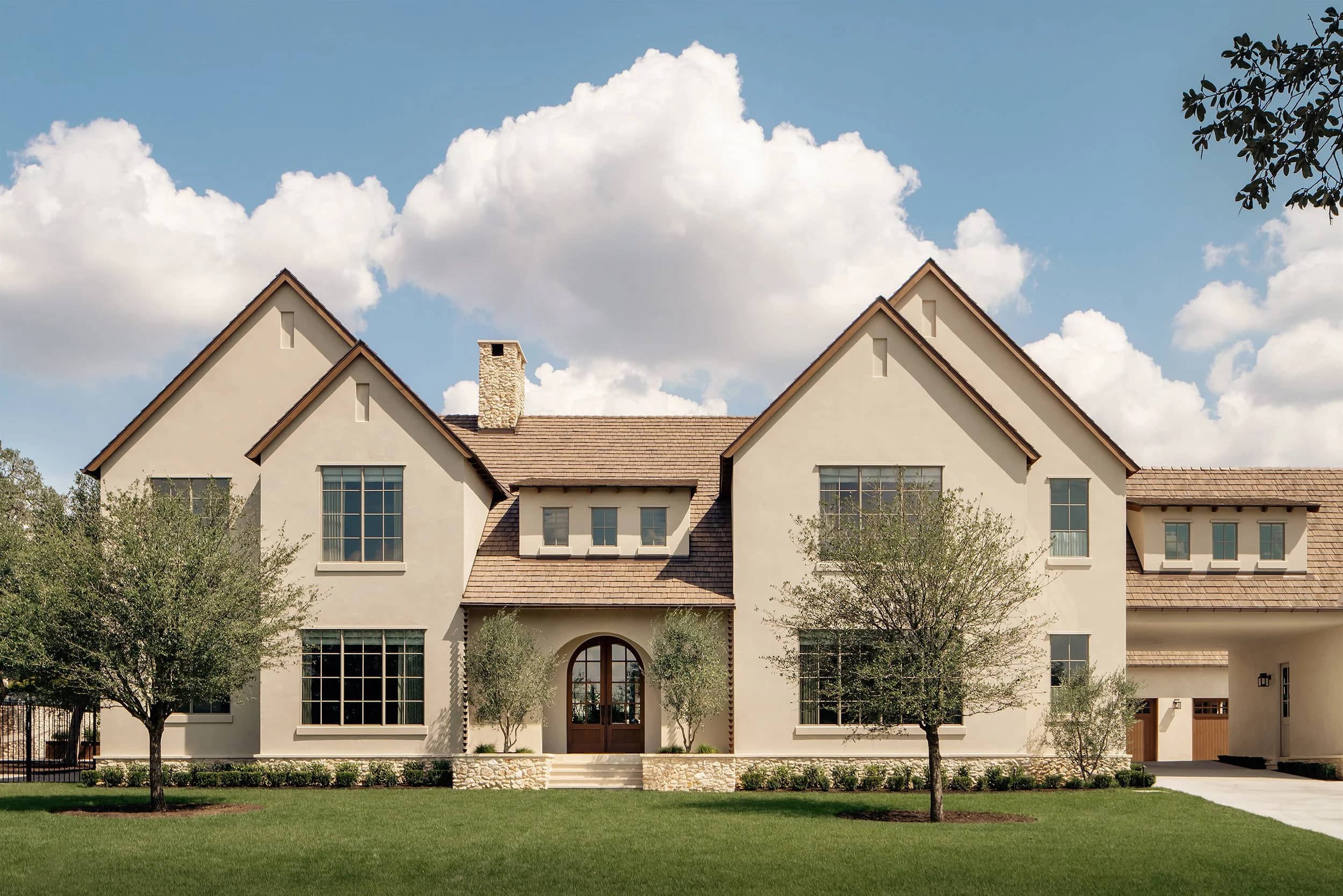 A limestone and stucco residence with steep gables and olive trees along the front elevation.